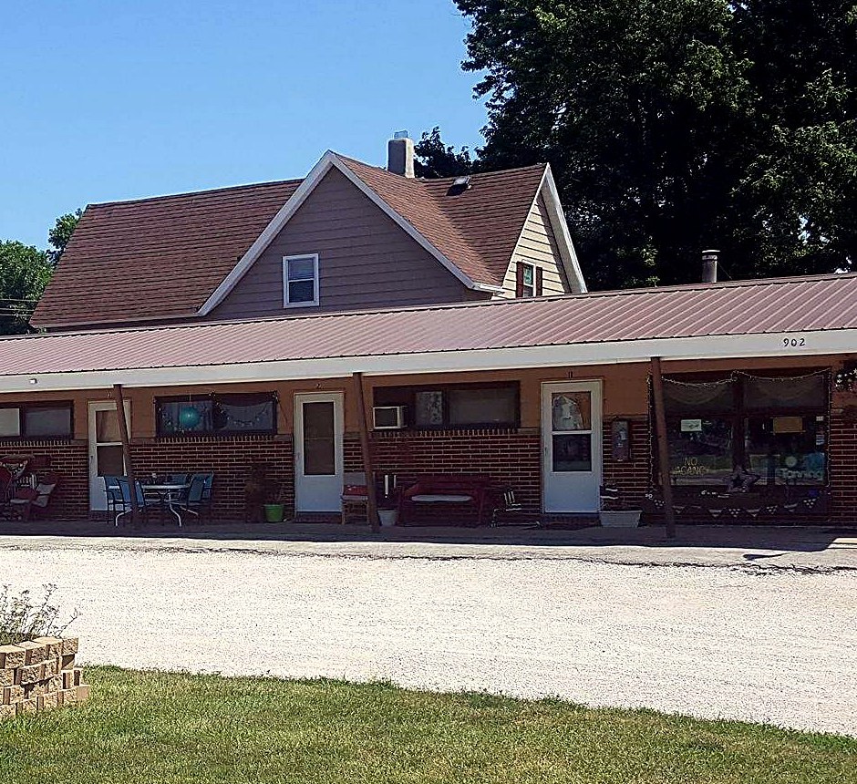 The Janco Motel building in Grand Junction, Iowa — a single-story brick motel with room doors opening onto the parking court and front lawn, seen on a summer day